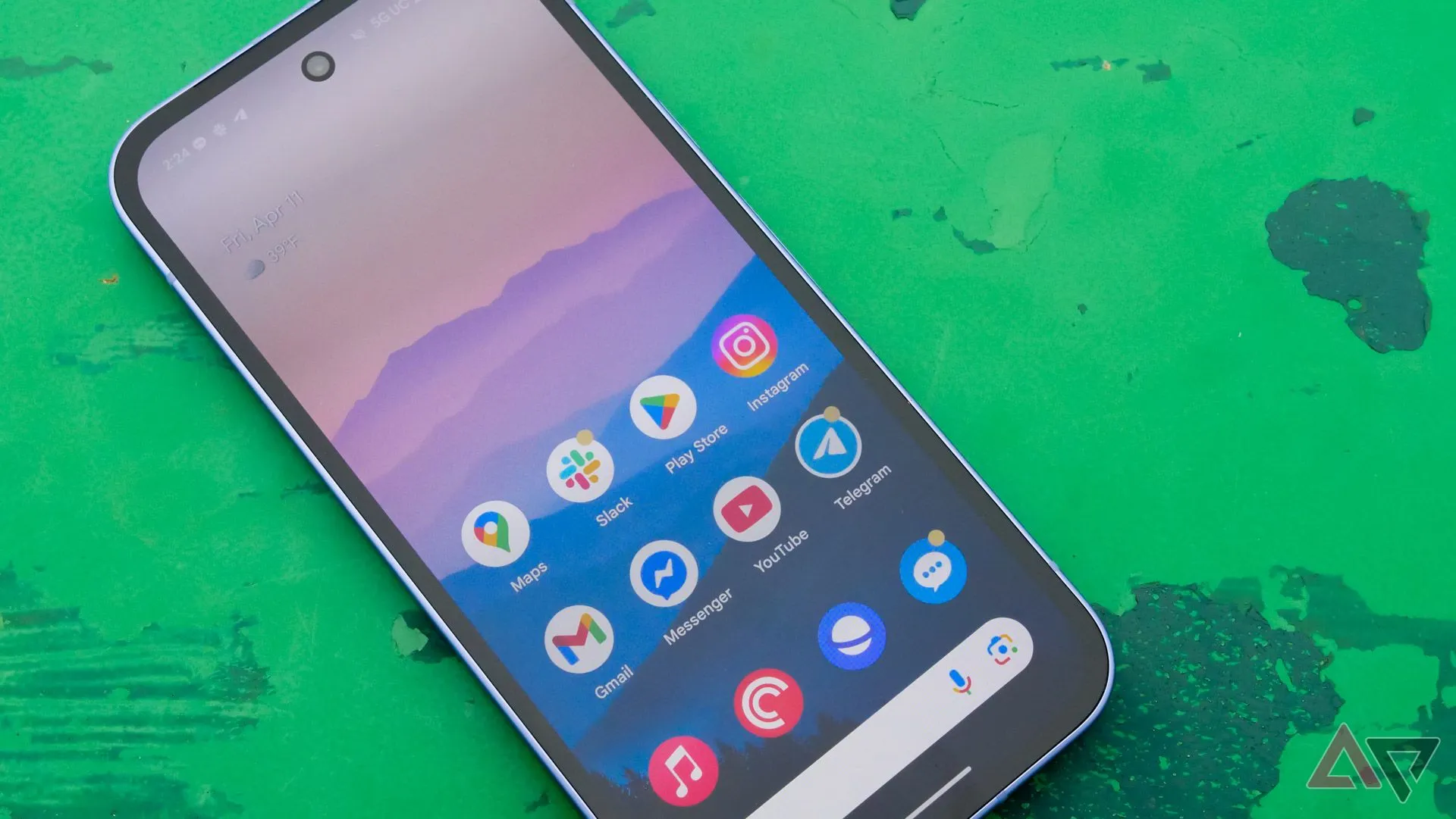 Điện thoại Google Pixel 9a đặt màn hình hướng lên trên bàn xanh ngoài trời.