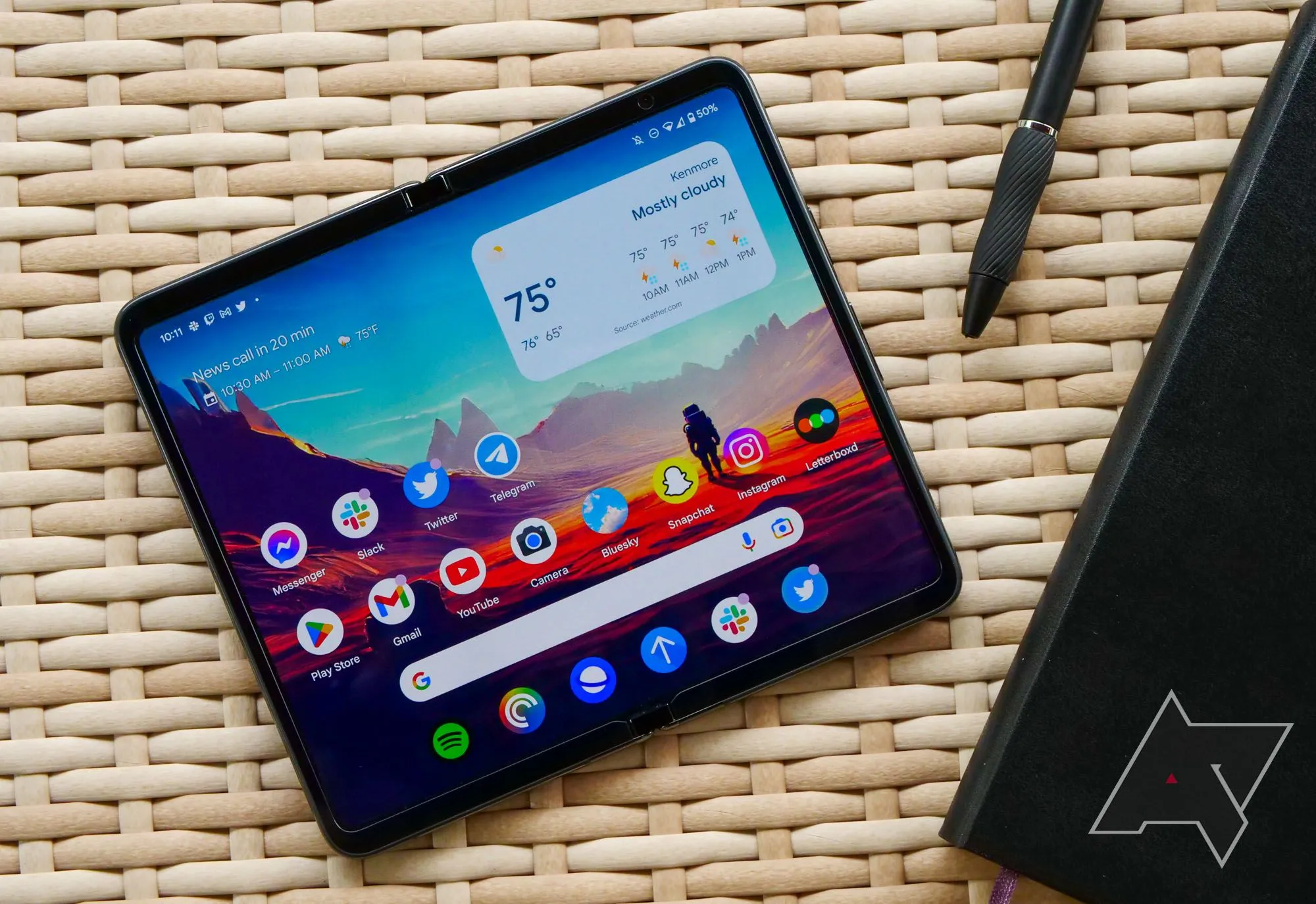 Điện thoại Google Pixel Fold đặt trên bàn mây tre cùng sổ tay và bút