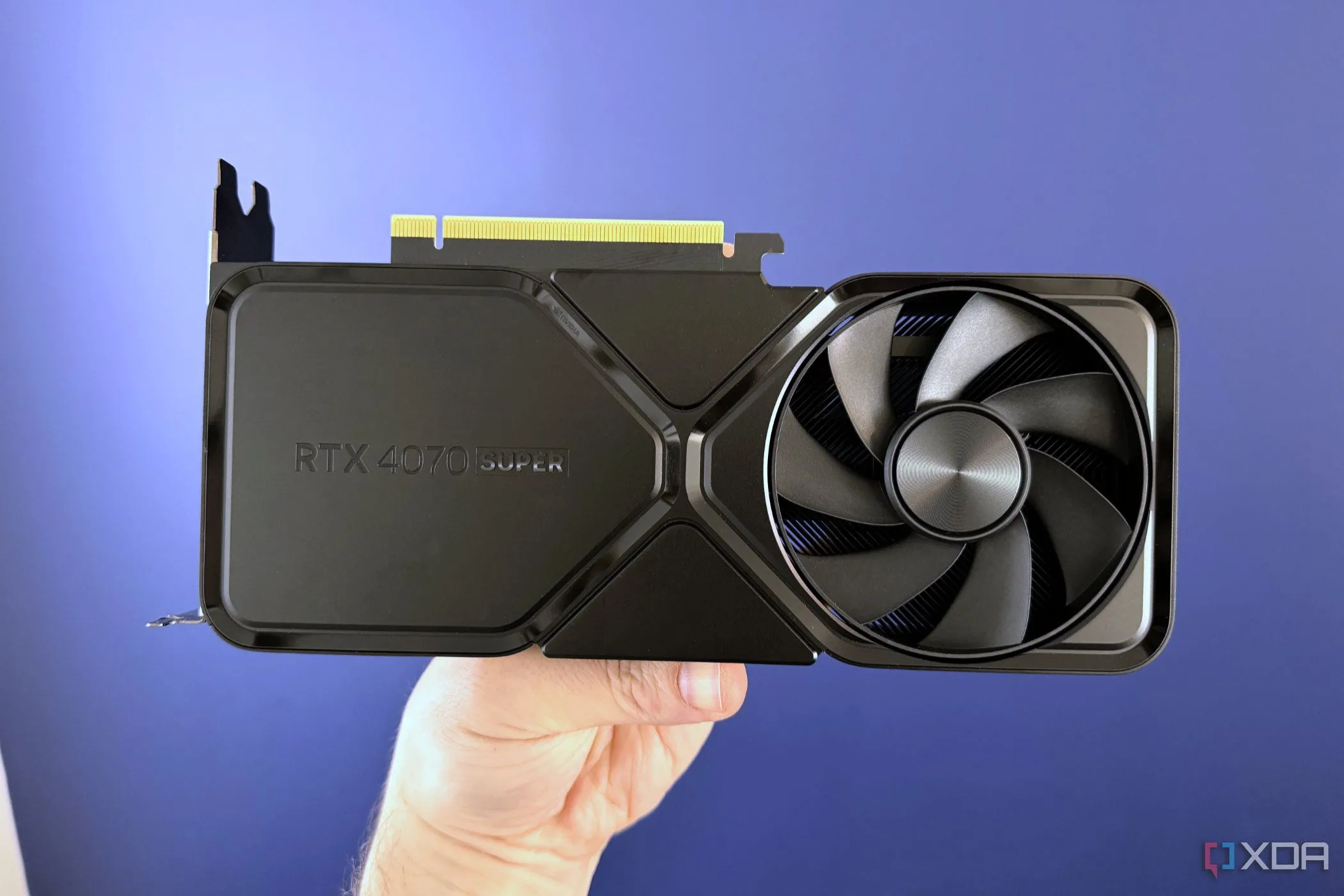 Card đồ họa NVIDIA GeForce RTX 4070 Super Founders Edition được cầm trước bức tường xanh, so sánh với RTX 5070