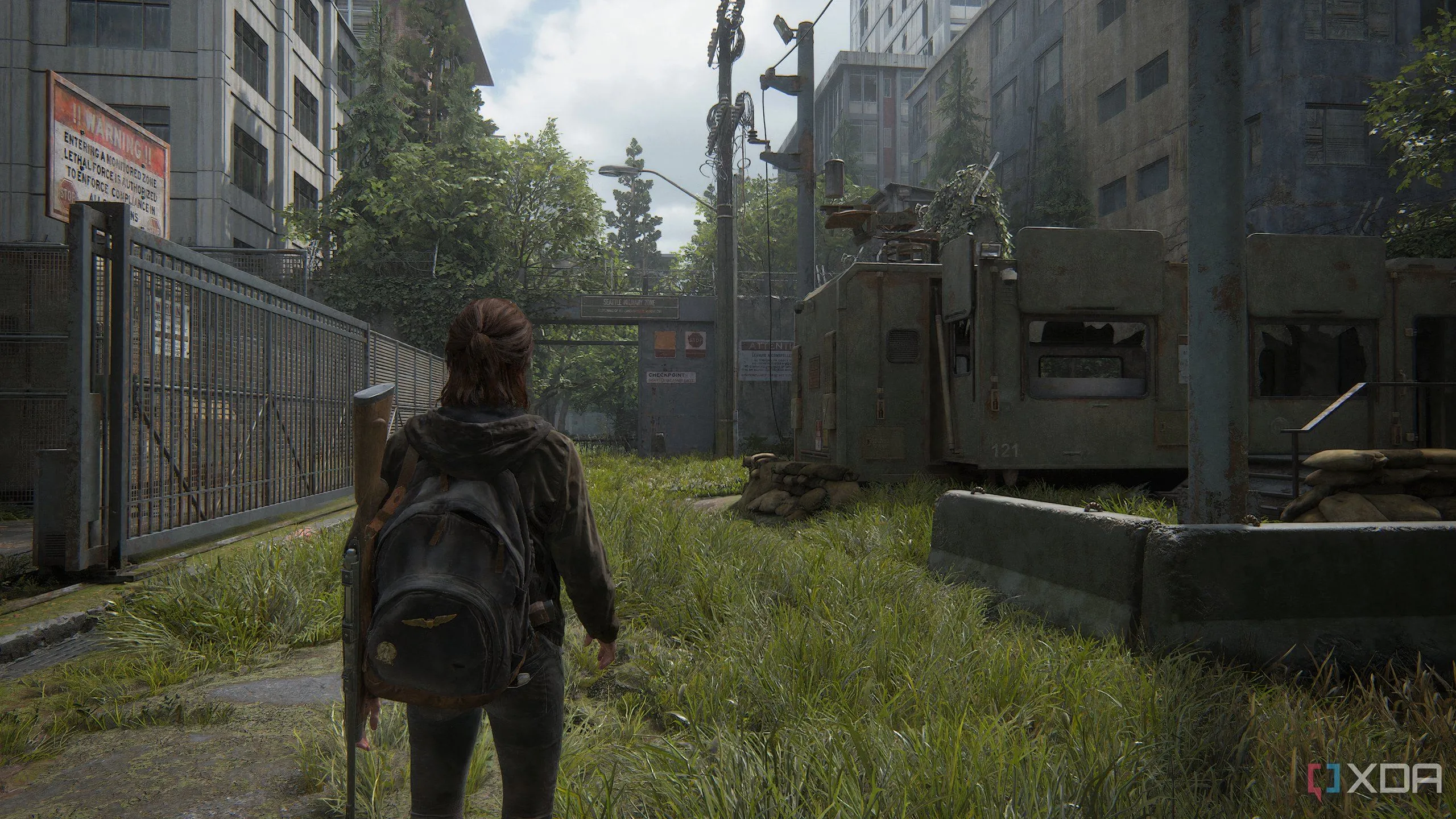 Ellie đi qua khu quân sự bị bỏ hoang trong The Last of Us Part II Remastered, thể hiện chi tiết đồ họa môi trường và ánh sáng ấn tượng của game trên PC.
