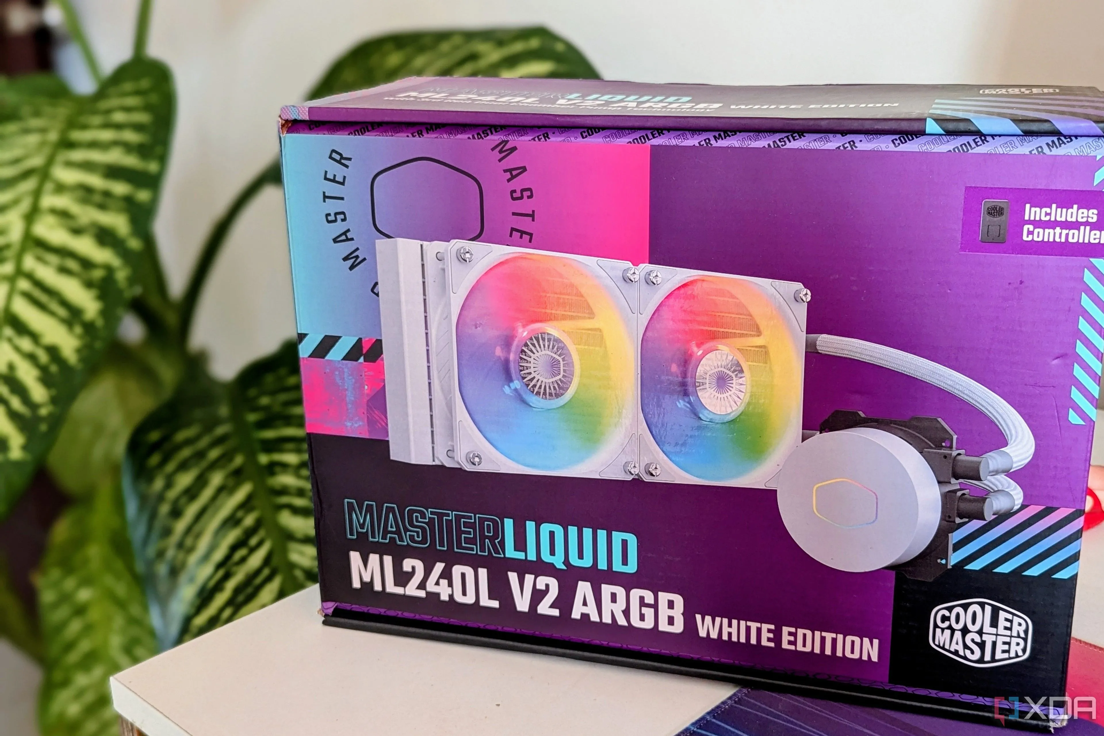 Hộp của bộ tản nhiệt chất lỏng AIO Cooler Master đặt trên bàn làm việc cạnh một chậu cây xanh, minh họa giải pháp làm mát cao cấp cho CPU