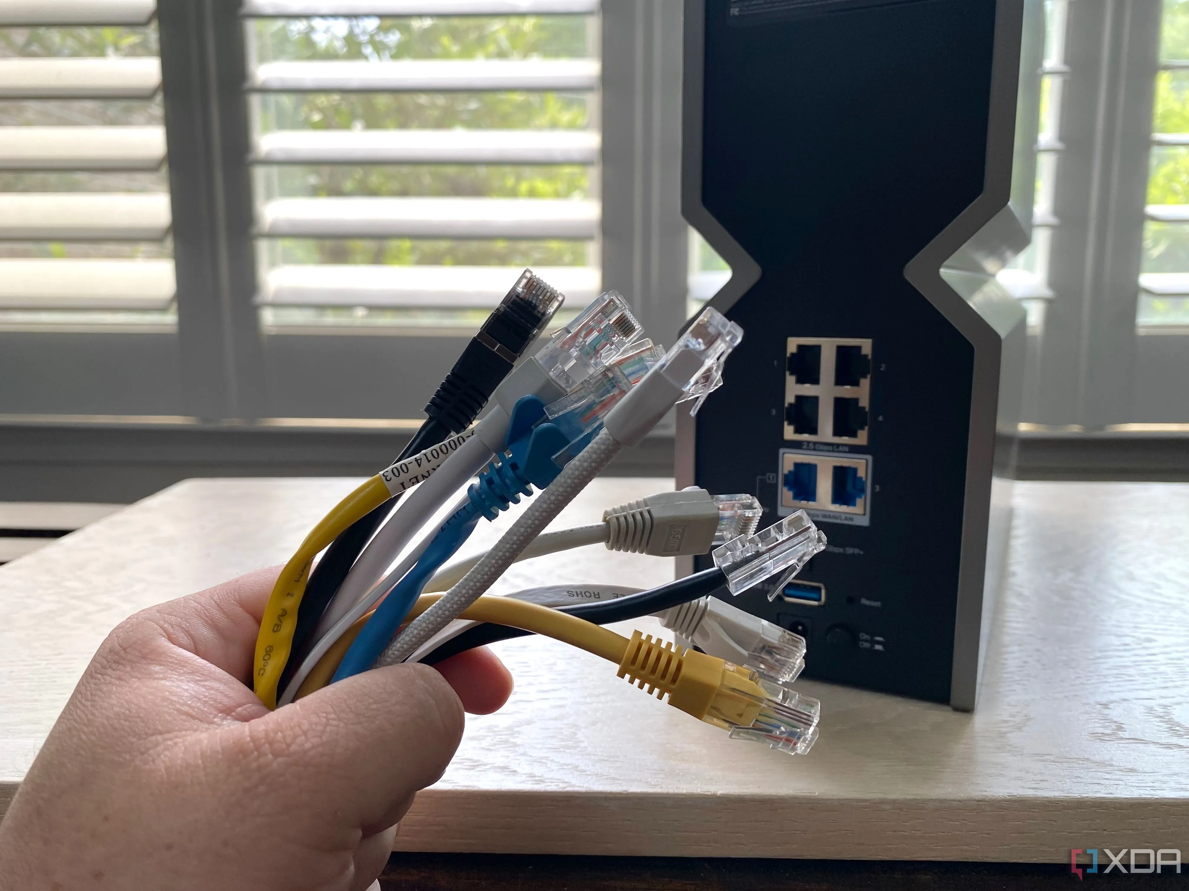 Một bó cáp Ethernet nhiều màu sắc đặt trước bộ định tuyến (router), minh họa phương pháp kết nối mạng có dây ổn định.