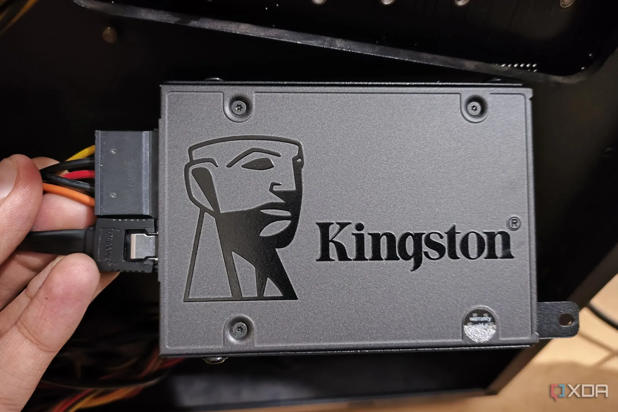 Một người đang cầm ổ cứng SSD có cáp nguồn và dữ liệu SATA được cắm, minh họa cho giải pháp tăng cường bộ nhớ tạm thời.