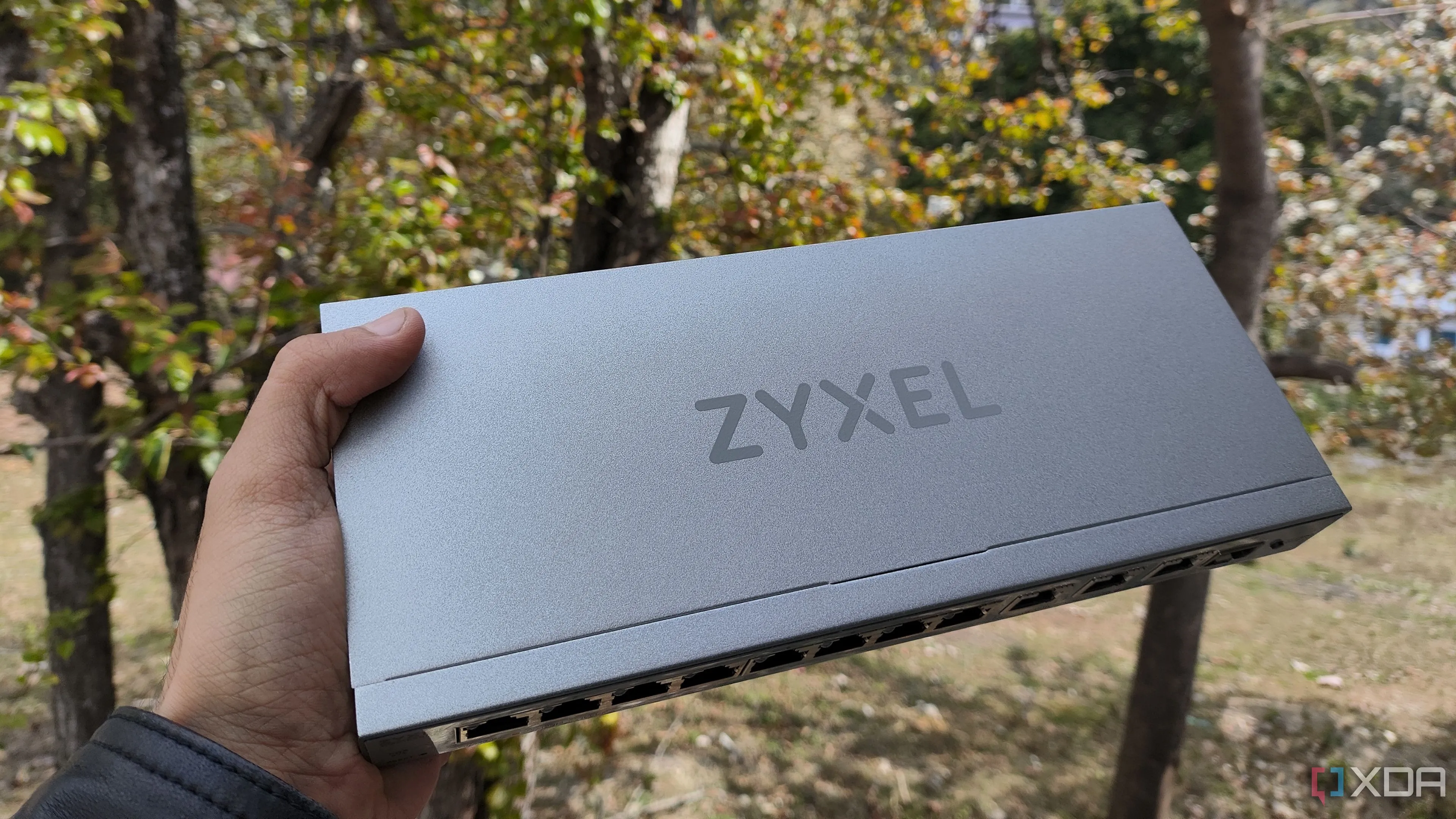 Một người đang cầm switch mạng Zyxel, biểu thị khả năng truyền dẫn tín hiệu và độ bền của thiết bị