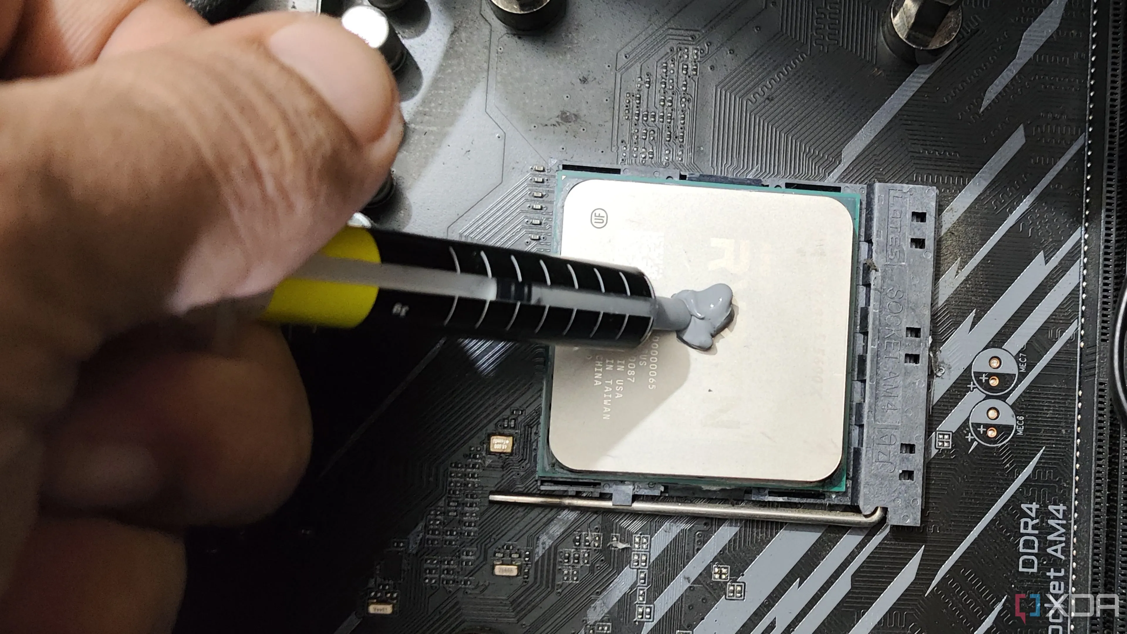 Một người đang thoa keo tản nhiệt mới lên CPU Ryzen 5 5600X, giúp truyền nhiệt hiệu quả và giảm nhiệt độ để tối ưu hiệu suất chơi game