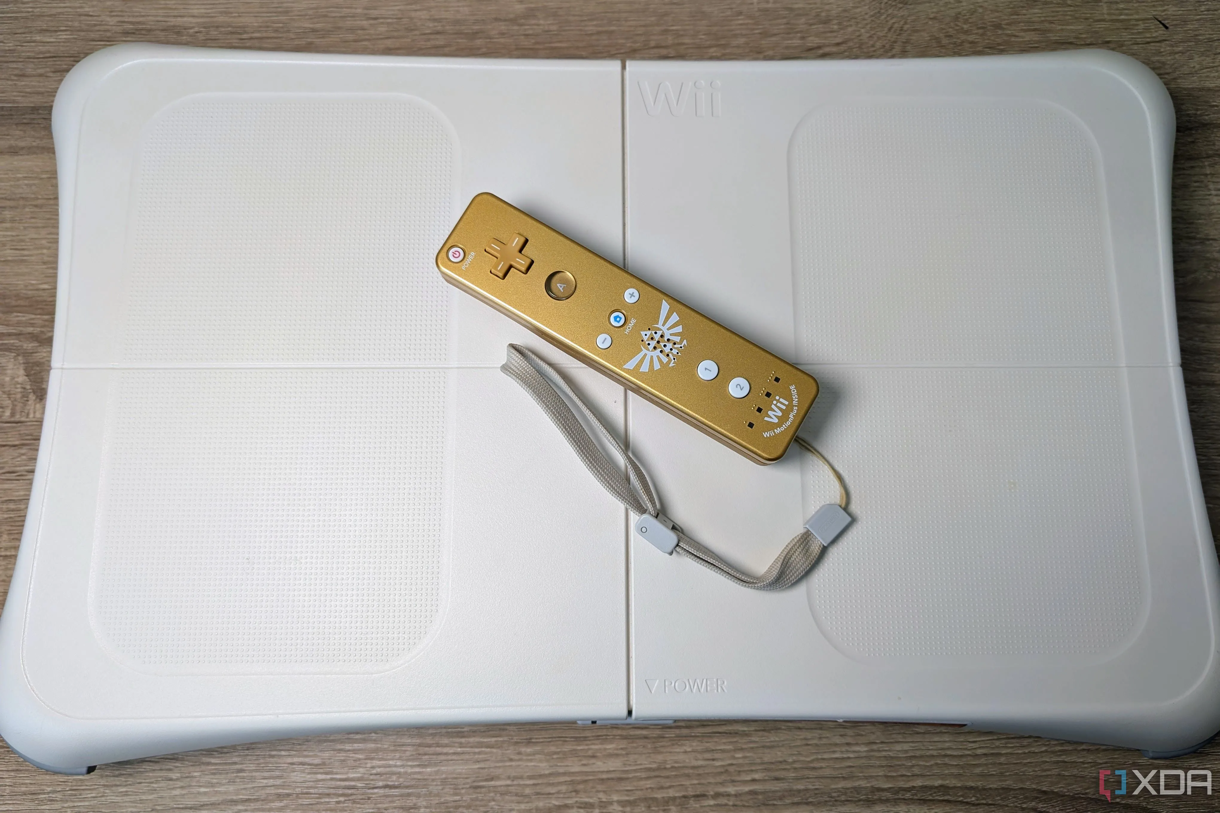Thiết bị Wii Balance Board màu trắng kèm tay cầm Wii-mote vàng trên nền sàn gỗ