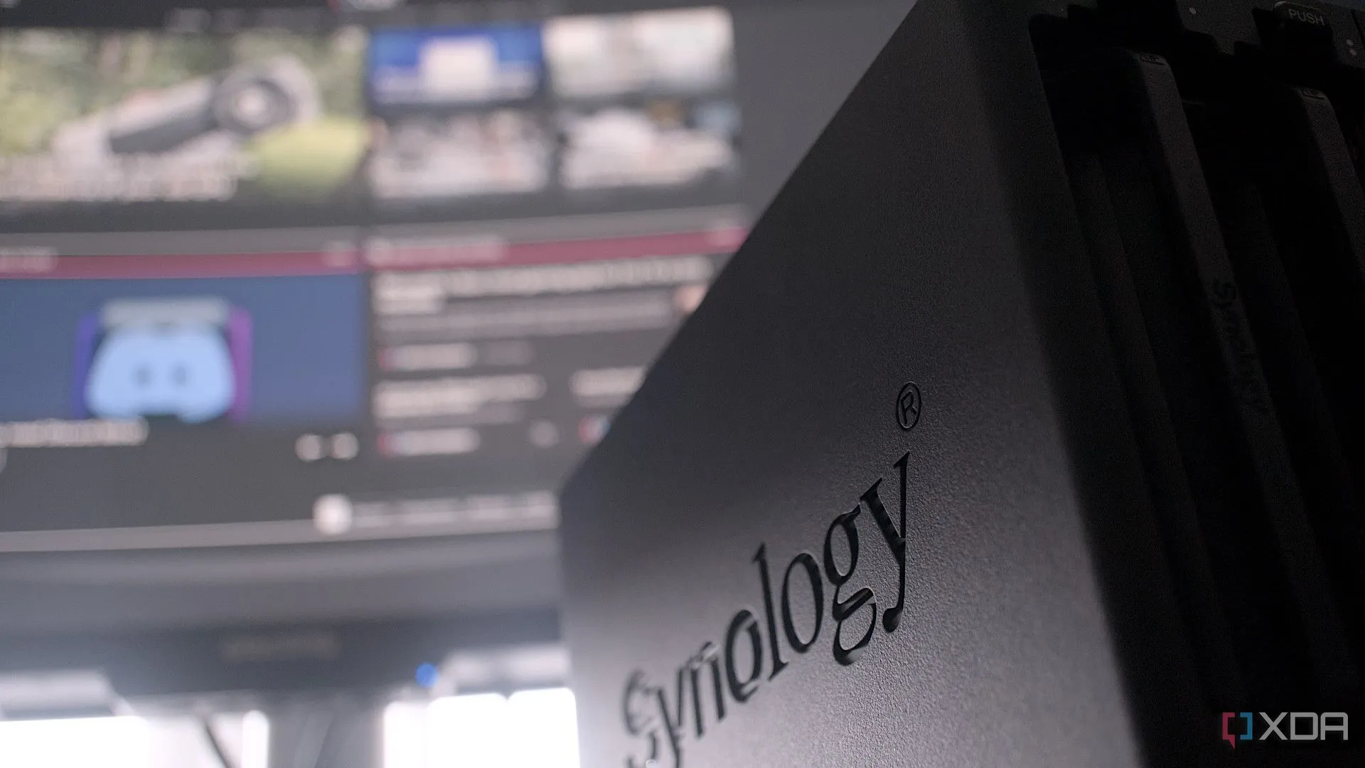 Trang web XDA Developers hiển thị trên màn hình kết nối với thiết bị NAS Synology, tượng trưng cho việc tự host dịch vụ.